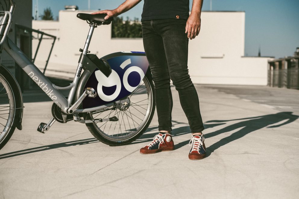 Die Beine eines Mannes neben einem nextbike-Leihfahrrads. Eine Hand liegt auf dem Sattel.